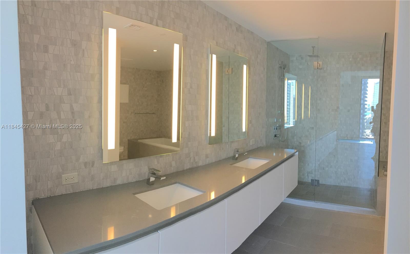 A modern bathroom features a double vanity with white cabinets, gray countertops, and illuminated mirrors — 88 SW 7th St # 2305, Miami FL 33130, MIAMI, FL