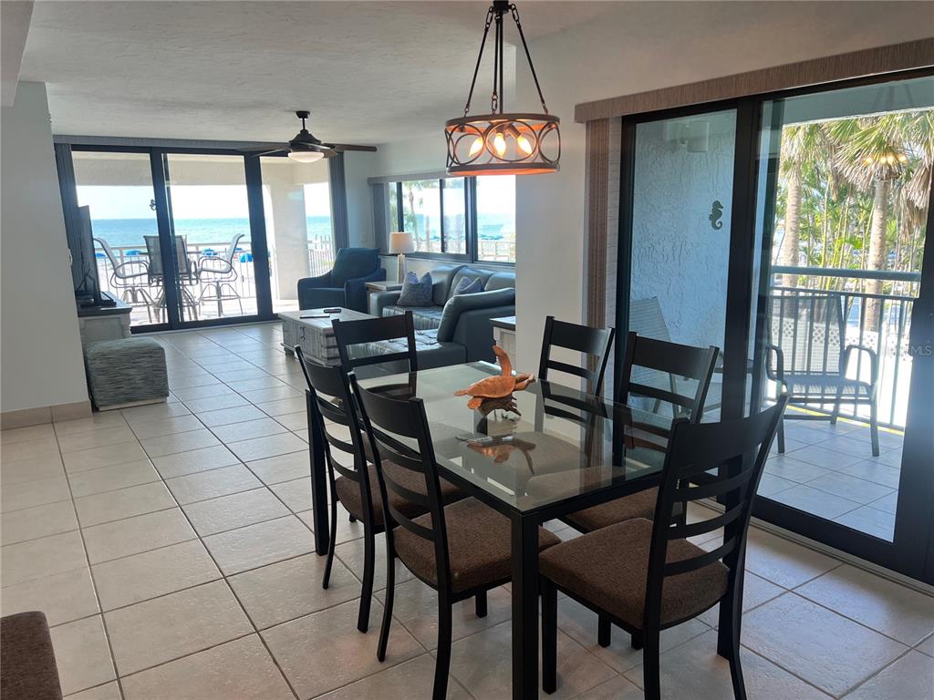 A dining area with a glass table and chairs overlooks a living room and ocean view — 1001 POINT OF ROCKS ROAD UNIT 212, SARASOTA, FL