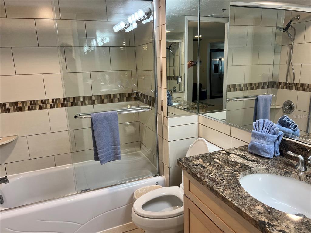 A bathroom features a tiled tub-shower combination, a granite vanity, and a toilet — 1001 POINT OF ROCKS ROAD UNIT 212, SARASOTA, FL