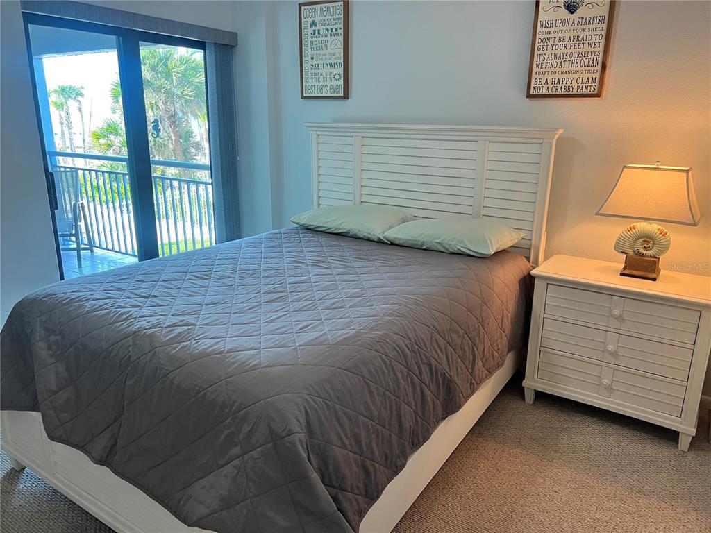 A bedroom features a white bed frame, gray quilted bedding, and a balcony with palm trees — 1001 POINT OF ROCKS ROAD UNIT 212, SARASOTA, FL