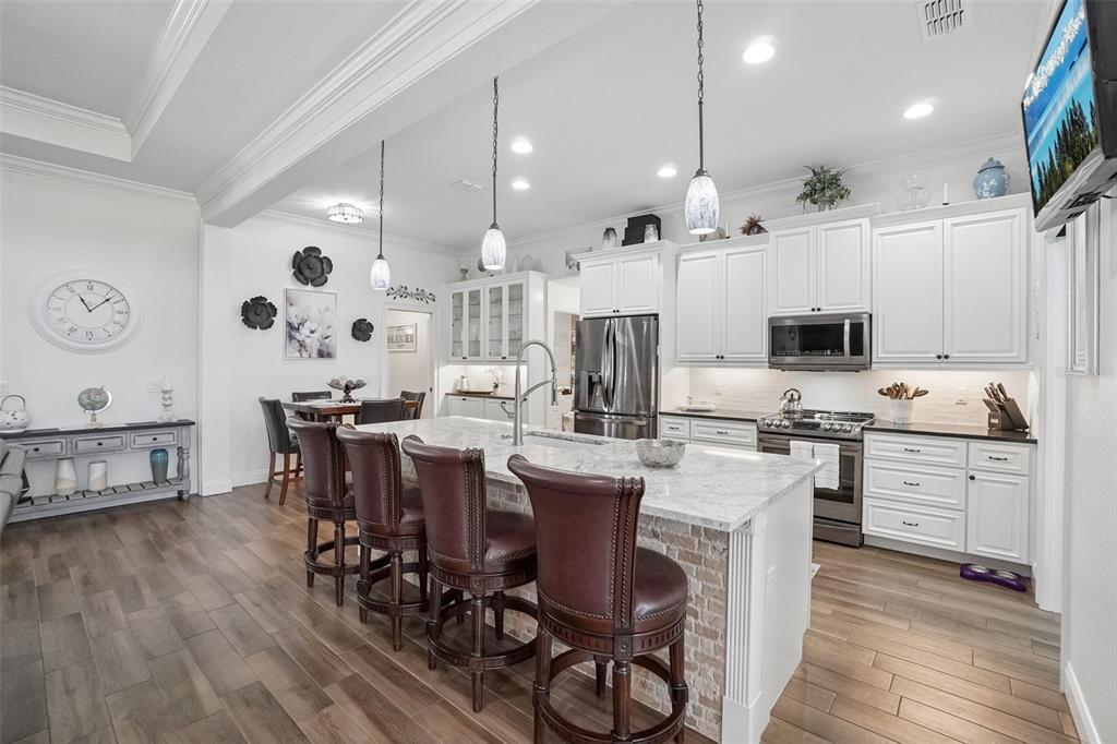 A kitchen features white cabinets, a granite-topped island with bar stools, and wood-look flooring — 3934 CONNERSVILLE ROAD, BARTOW, FL
