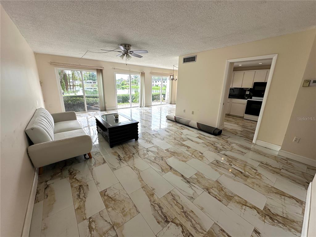 A living room features white marble-look tile flooring, a beige sofa, and glass sliding doors — 1655 S HIGHLAND AVENUE UNIT J190, CLEARWATER, FL