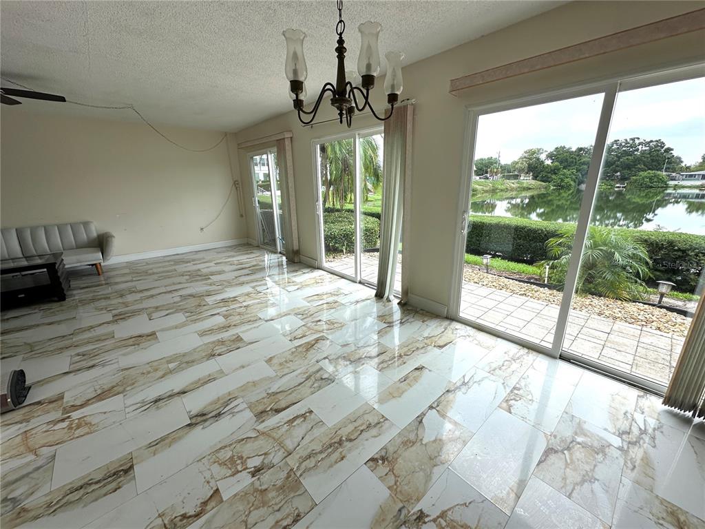 A bright living area features white marble-look tile flooring, a chandelier, and sliding glass doors — 1655 S HIGHLAND AVENUE UNIT J190, CLEARWATER, FL