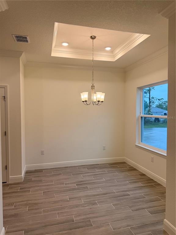 A dining area features a tray ceiling, a chandelier, and wood-look tile flooring — 13412 BREWSTER ROAD, SPRING HILL, FL