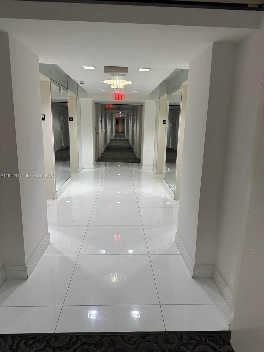 A long, white-tiled hallway features mirrored walls and recessed lighting leading to an exit sign — 350 S Miami Ave # 2913, Miami FL 33130, MIAMI, FL