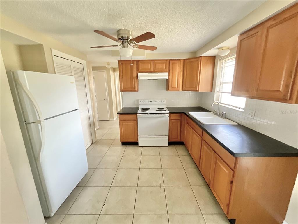 A kitchen features wood cabinets, black countertops, white appliances, and light-colored tile flooring — 3528 LATIMER STREET, NEW PORT RICHEY, FL