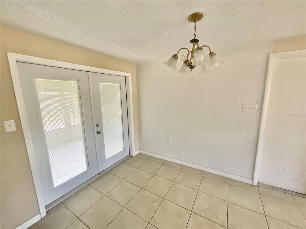 A dining area features tile flooring, a white brick wall, and a multi-light chandelier — 3528 LATIMER STREET, NEW PORT RICHEY, FL