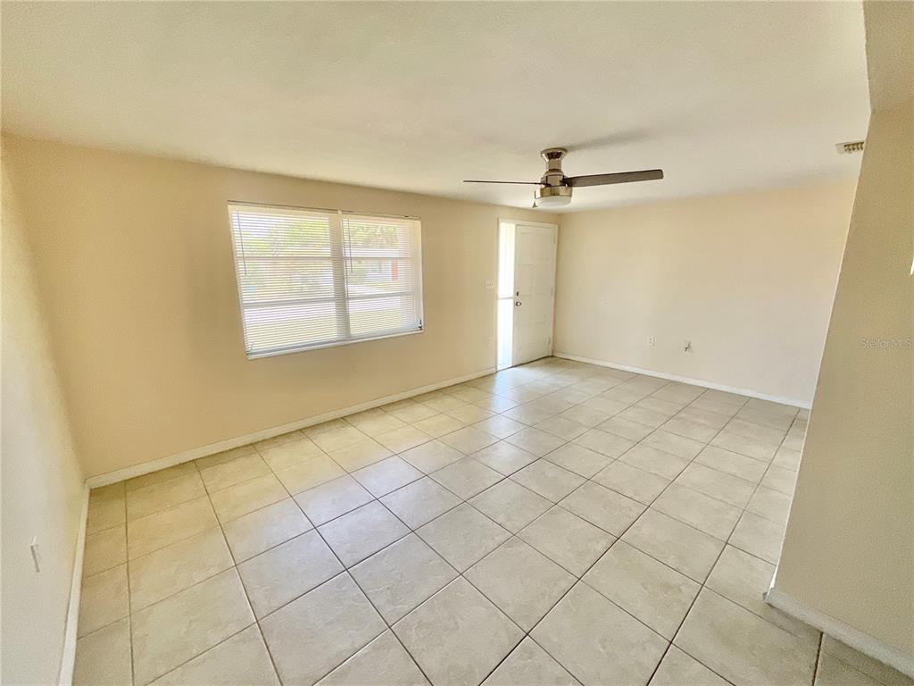 A living room with beige walls, light-colored tile flooring, a ceiling fan, and a window — 3528 LATIMER STREET, NEW PORT RICHEY, FL