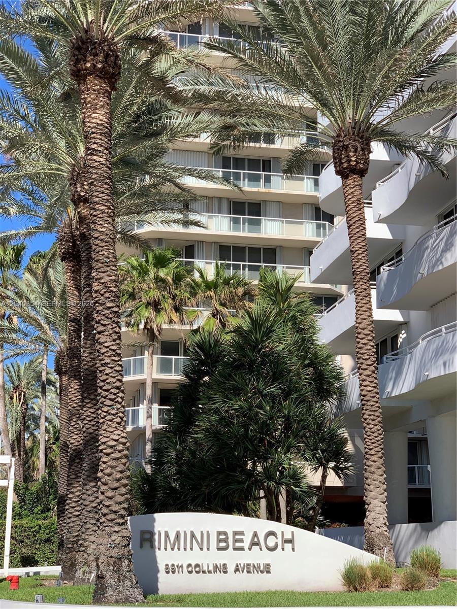 A low-angle view shows a multi-story apartment building behind palm trees and a signage monument — 8911 Collins Ave # 505, Surfside FL 33154, SURFSIDE, FL