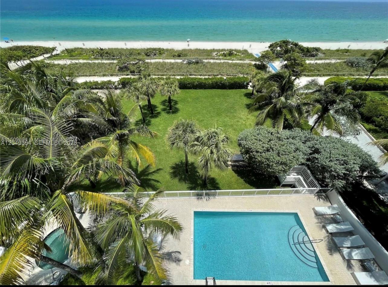 An elevated view of a swimming pool, palm trees, a grassy lawn, and the ocean beach — 8911 Collins Ave # 505, Surfside FL 33154, SURFSIDE, FL