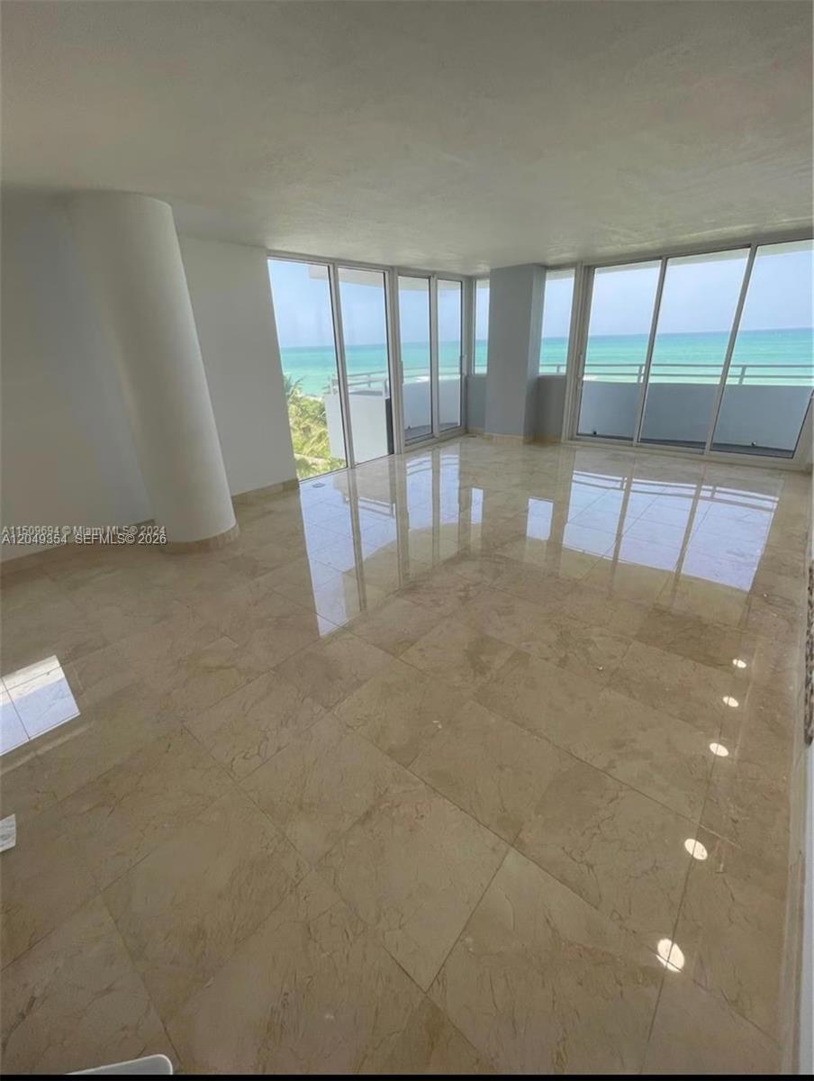 An empty room with beige tile flooring and floor-to-ceiling windows overlooking the ocean — 8911 Collins Ave # 505, Surfside FL 33154, SURFSIDE, FL