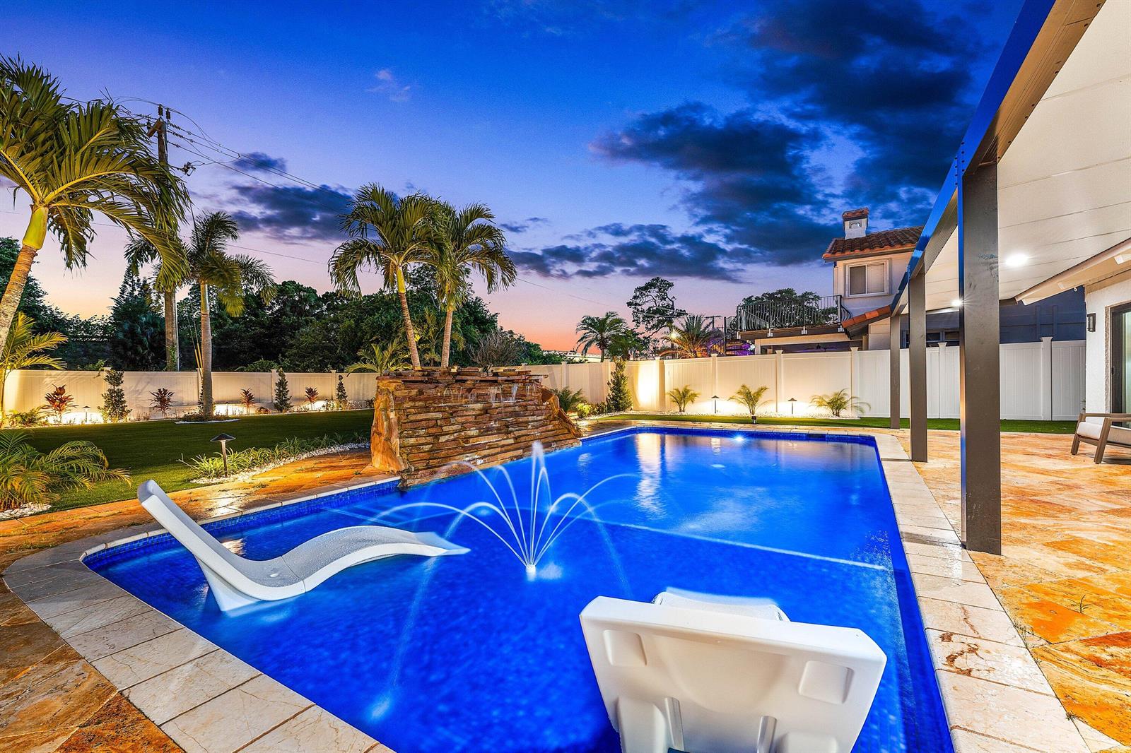 A backyard swimming pool features a stone waterfall, fountain, and two lounge chairs at dusk — 1520 SW 17th Street, Boca Raton FL 33486, BOCA RATON, FL