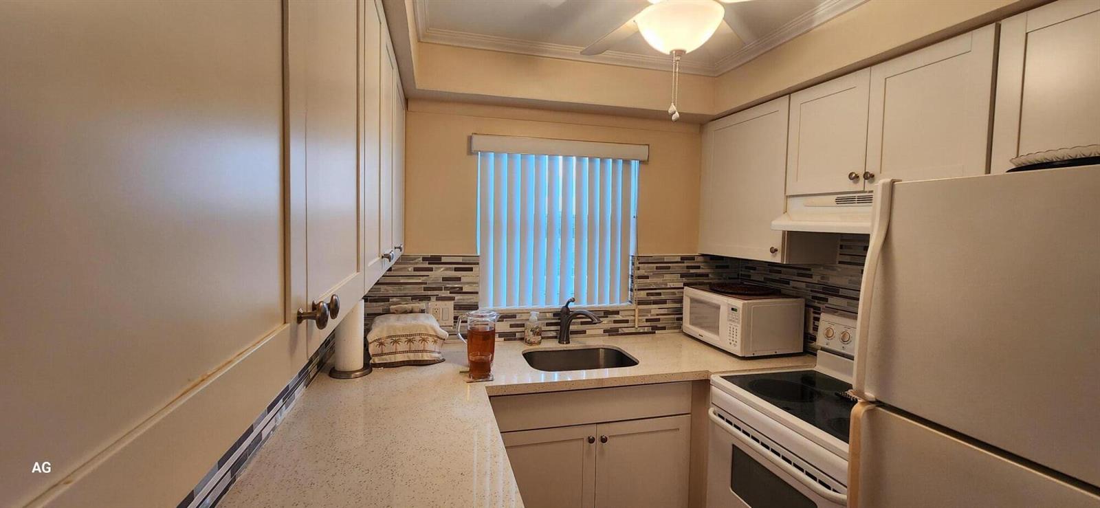 A galley kitchen features white cabinets, a tiled backsplash, and a stainless steel sink — 15 SE 13th Street # D3, Boca Raton FL 33432, BOCA RATON, FL