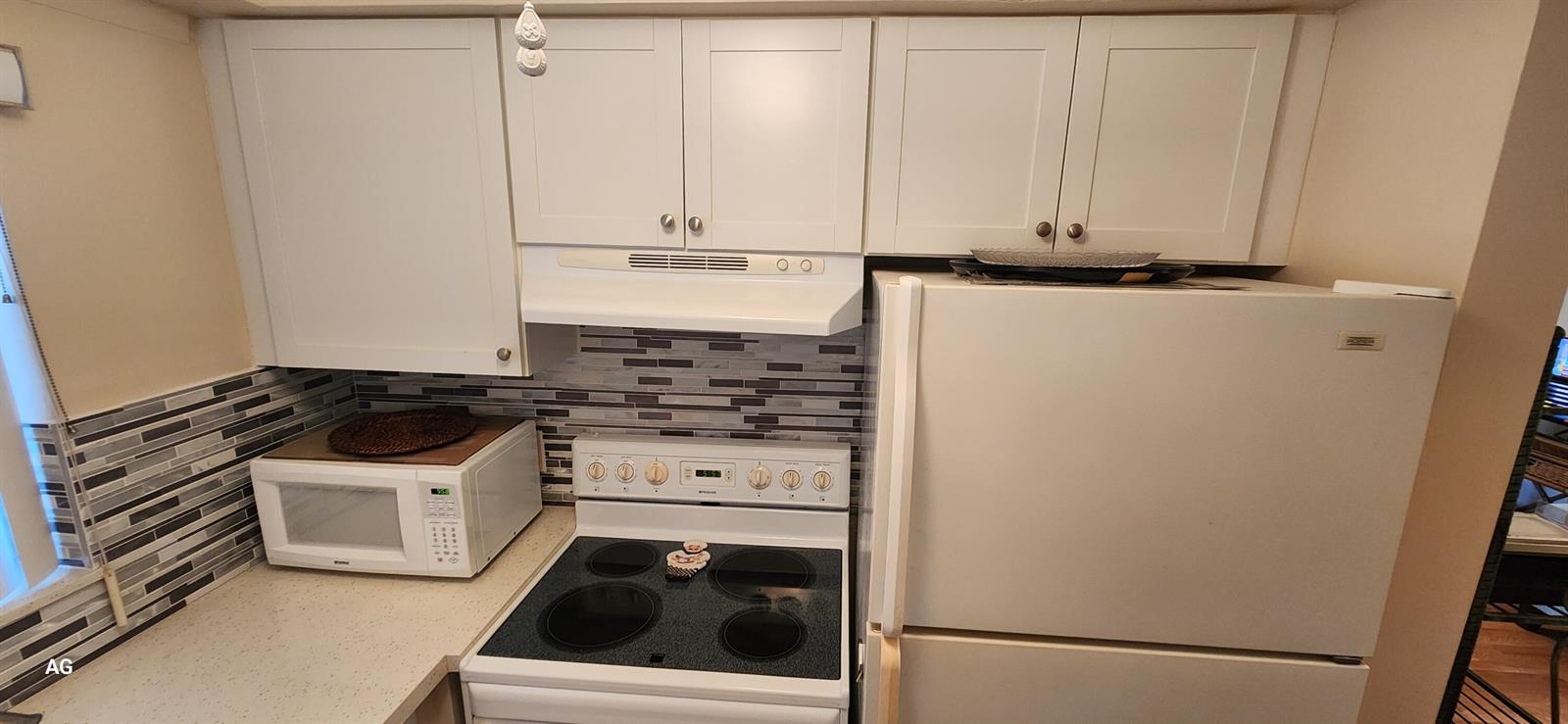 A kitchen features white cabinets, a white stove, a microwave, and a tiled backsplash — 15 SE 13th Street # D3, Boca Raton FL 33432, BOCA RATON, FL