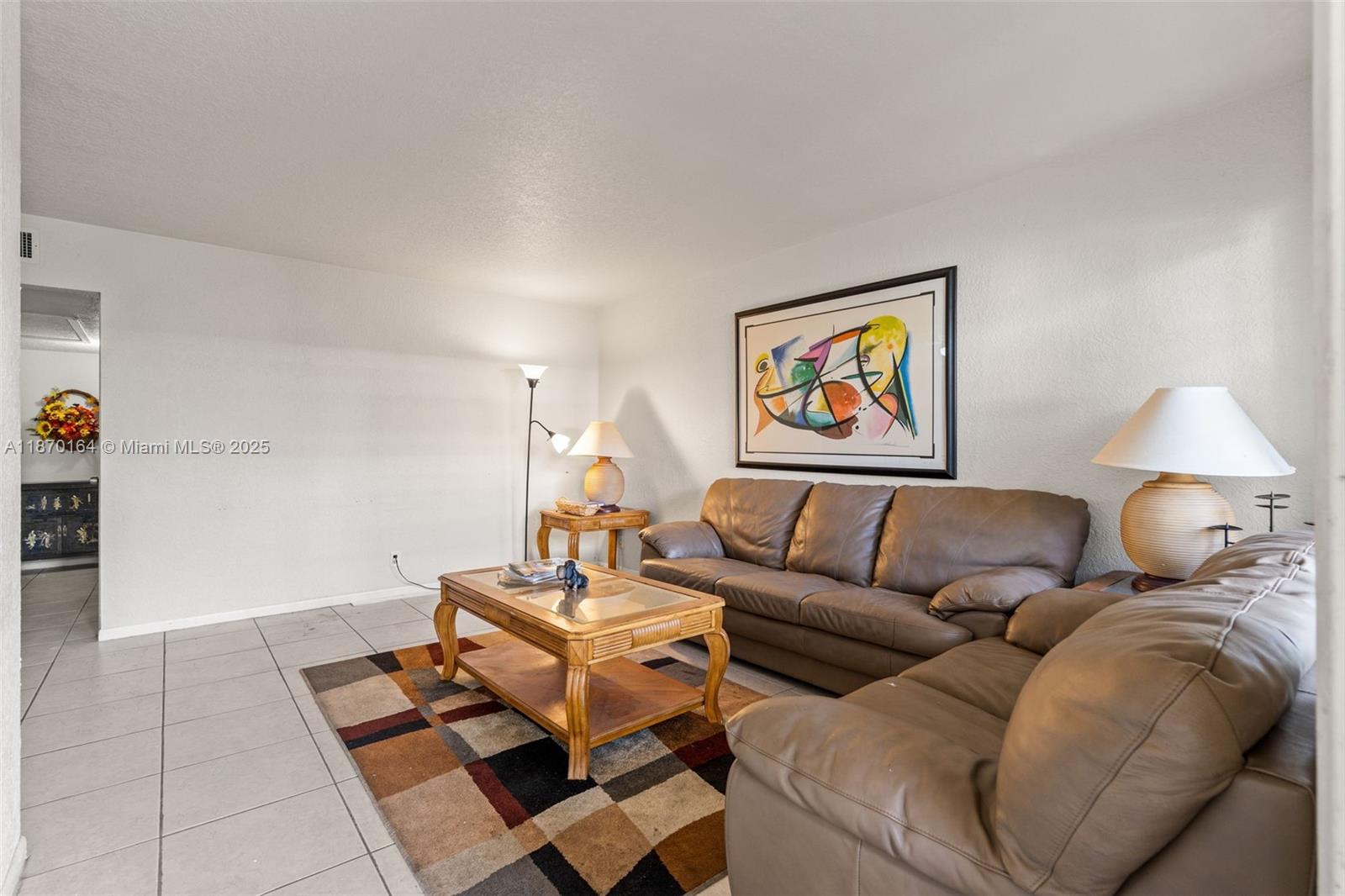 A living room features a brown leather sectional, a wooden coffee table, and abstract wall art — 200 Croton Ave # 104, Lantana FL 33462, LANTANA, FL