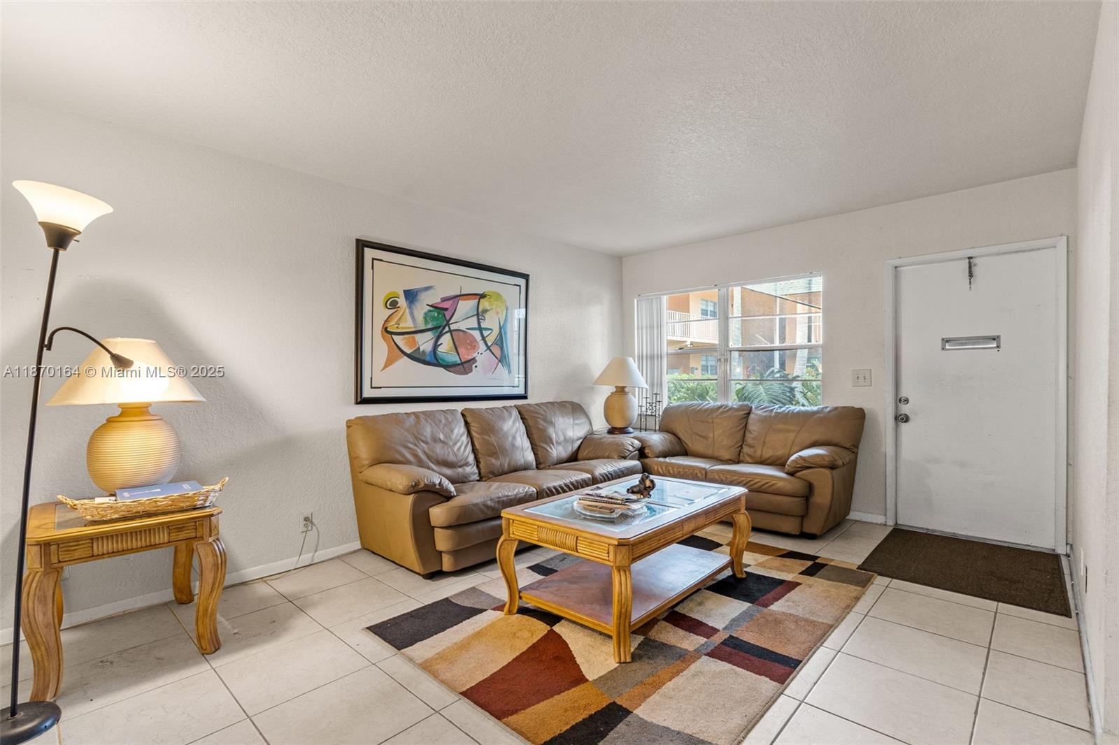 A living room features tan leather sofas, a glass-top coffee table, and tiled flooring — 200 Croton Ave # 104, Lantana FL 33462, LANTANA, FL