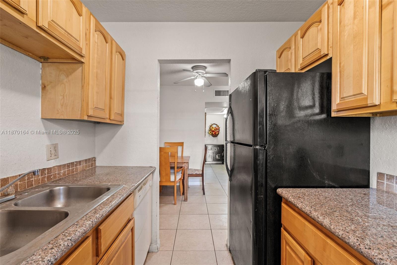 A kitchen features light wood cabinets, granite countertops, a black refrigerator, and a tiled floor — 200 Croton Ave # 104, Lantana FL 33462, LANTANA, FL