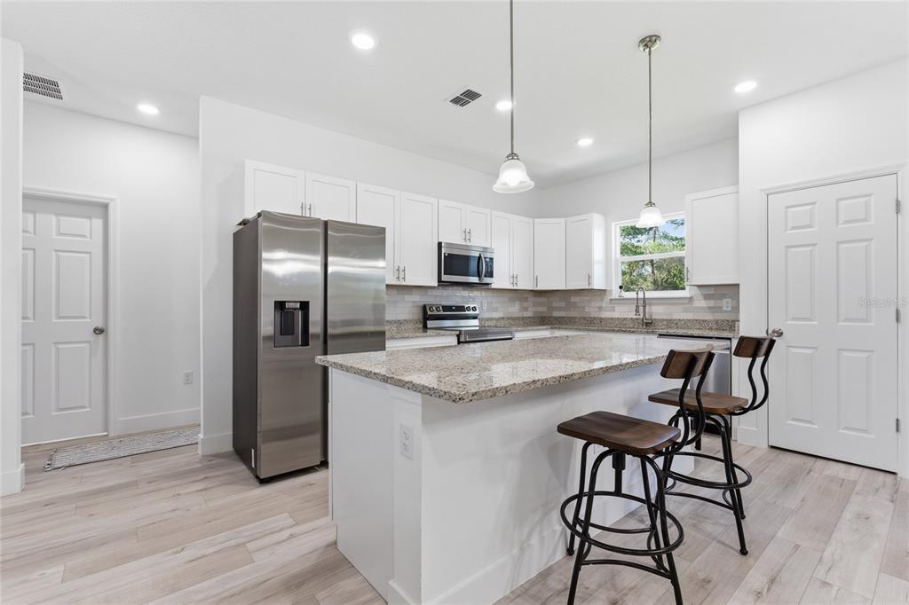 A modern kitchen features white cabinets, granite countertops, stainless steel appliances, and a breakfast island — 14 FISHER PLACE, OCKLAWAHA, FL