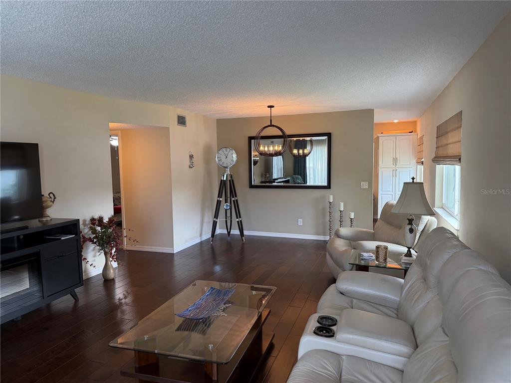 A living room features dark wood floors, a white leather sofa, and a tripod clock — 2426 ECUADORIAN WAY UNIT 40, CLEARWATER, FL