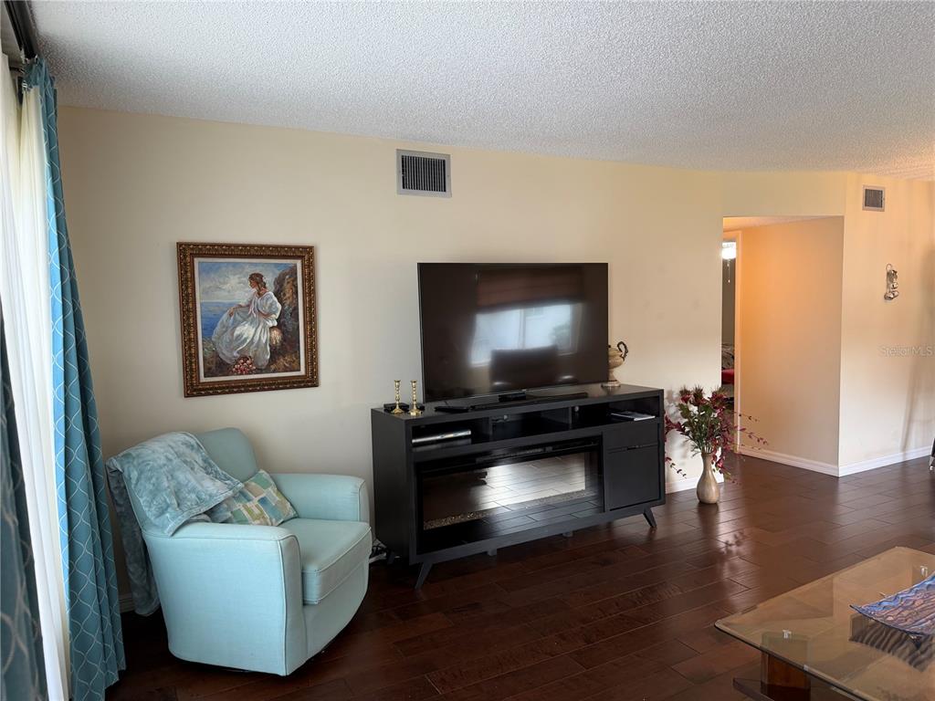 A living room features dark wood floors, a light blue armchair, and a television console — 2426 ECUADORIAN WAY UNIT 40, CLEARWATER, FL