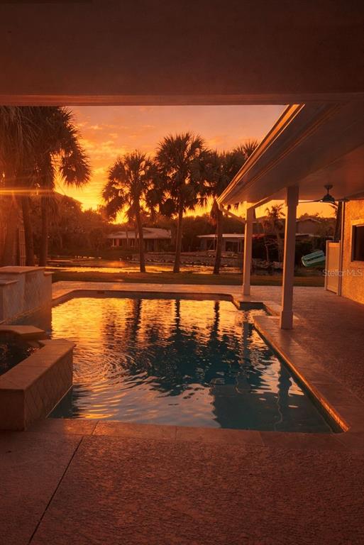 A swimming pool sits on a patio overlooking palm trees during a vibrant sunset — 4646 GLEASON AVENUE, SARASOTA, FL