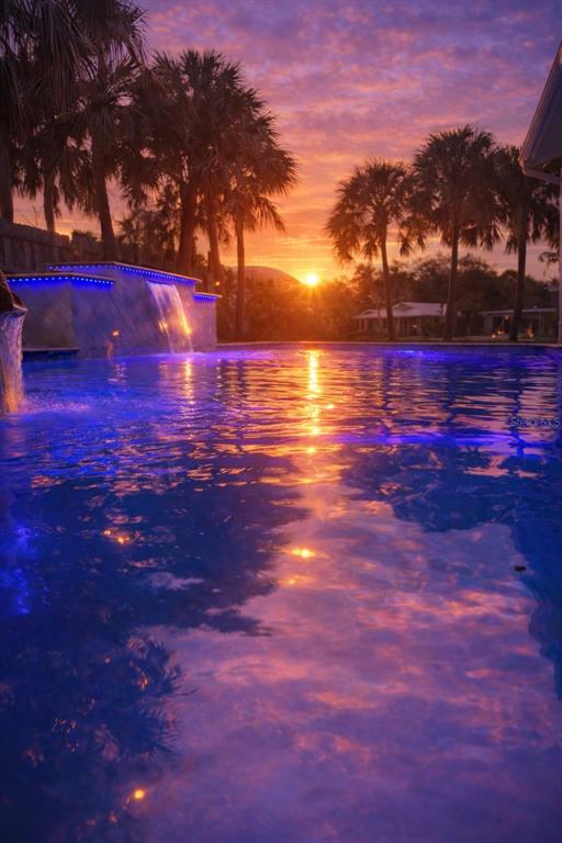 A swimming pool with a stone waterfall feature at sunset surrounded by palm trees — 4646 GLEASON AVENUE, SARASOTA, FL