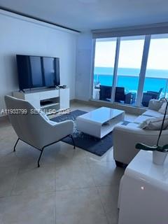 A living room features white furniture, a television, and a balcony overlooking the ocean — 2301 Collins Ave # 1025, Miami Beach FL 33139, MIAMI BEACH, FL