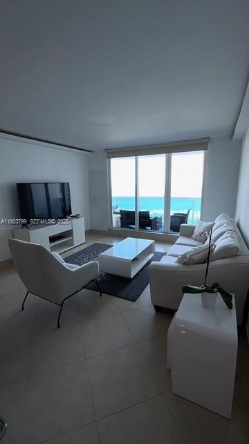 A modern living room features a white sofa, armchair, coffee table, and ocean view windows — 2301 Collins Ave # 1025, Miami Beach FL 33139, MIAMI BEACH, FL