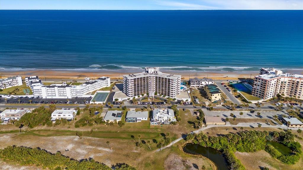 An aerial view shows a multi-story beachfront hotel surrounded by parking lots and coastal vegetation — 3580 OCEAN SHORE BOULEVARD UNIT 101, FLAGLER BEACH, FL