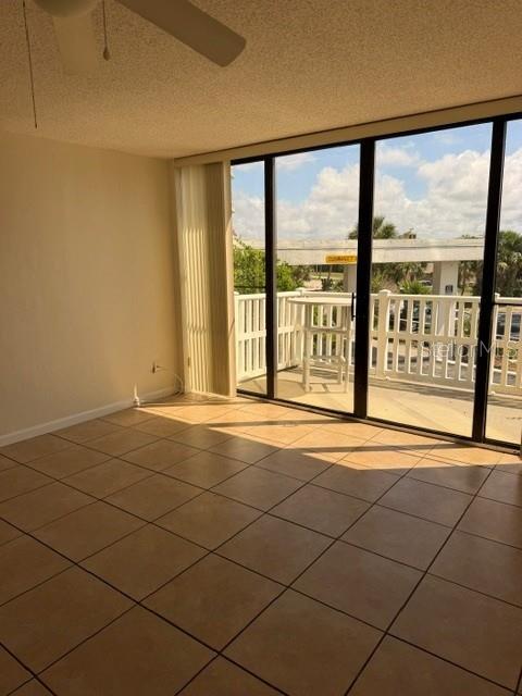 An empty room with tan tile flooring features a ceiling fan and large sliding glass doors — 3580 OCEAN SHORE BOULEVARD UNIT 101, FLAGLER BEACH, FL