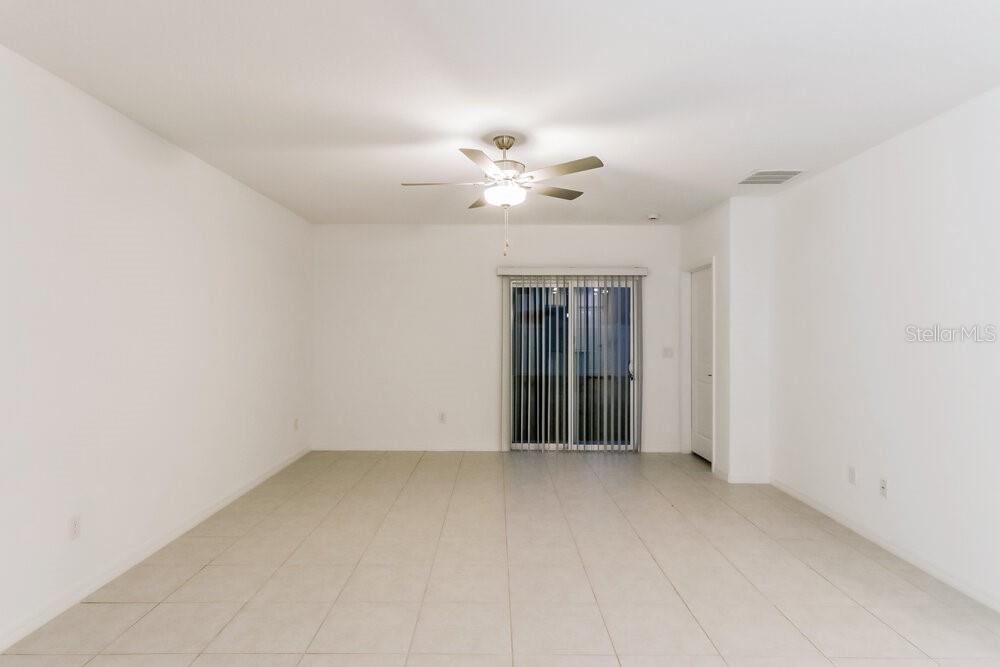 An empty room with white walls, tile flooring, a ceiling fan, and sliding glass doors — 17900 BEAMING RAYS LANE, LUTZ, FL