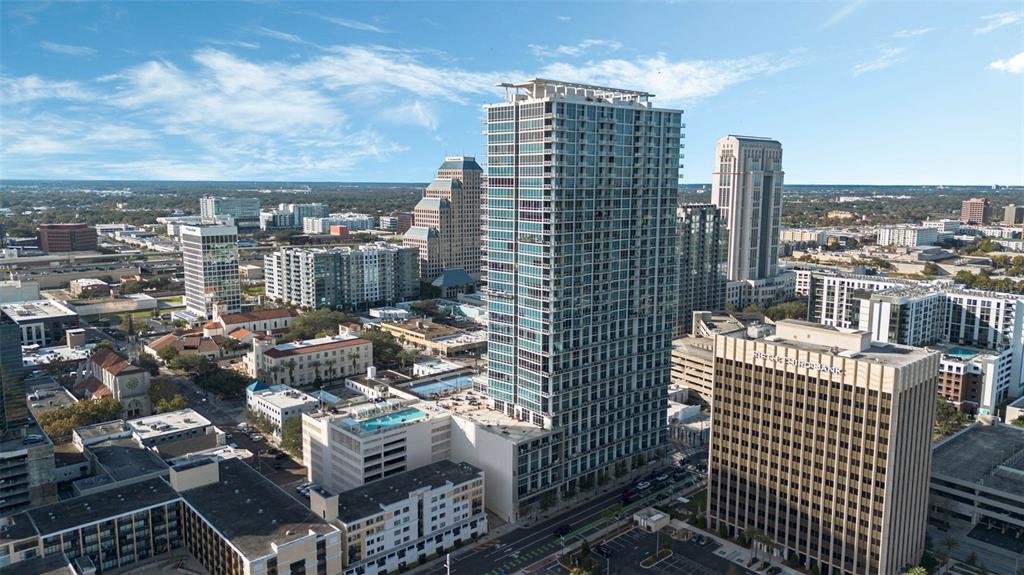 An aerial view of a tall glass skyscraper surrounded by other urban buildings and streets — 150 E ROBINSON STREET UNIT 3104-1, ORLANDO, FL