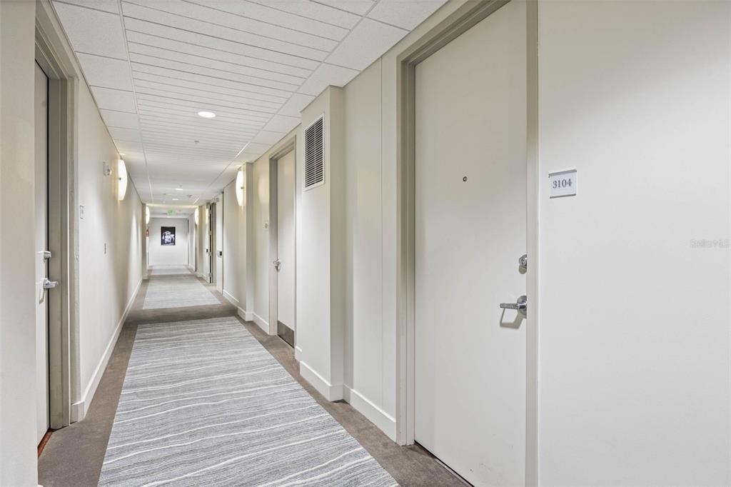 A long, carpeted hallway features white walls, recessed lighting, and several closed apartment doors — 150 E ROBINSON STREET UNIT 3104-1, ORLANDO, FL