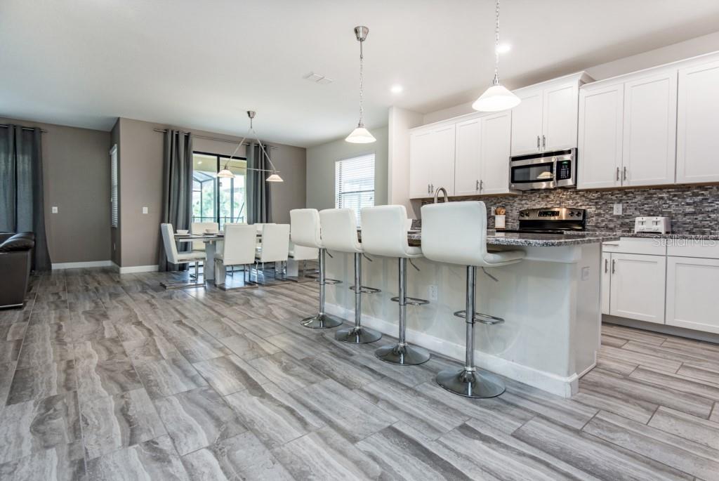 A kitchen with white cabinets, granite countertops, and a breakfast bar with four white stools — 5425 SOLTERRA CIRCLE, DAVENPORT, FL