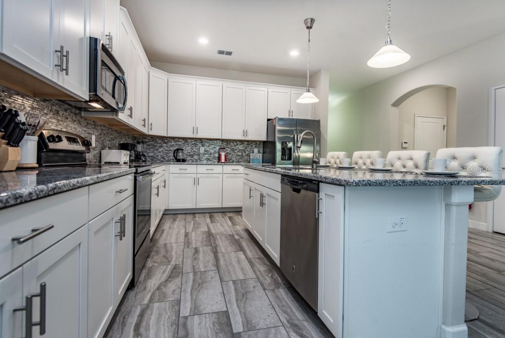 A modern kitchen features white cabinets, granite countertops, stainless steel appliances, and gray tile flooring — 5425 SOLTERRA CIRCLE, DAVENPORT, FL