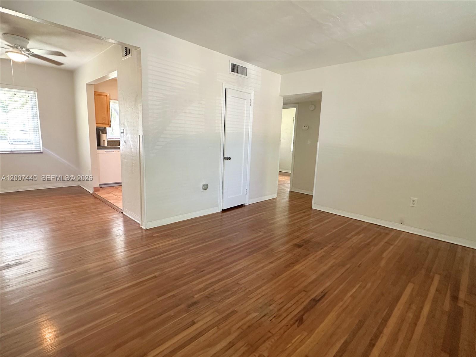 An empty living room features hardwood floors, white walls, and a doorway leading to a kitchen — 7734 SW 55th Ave # B, Miami FL 33143, MIAMI, FL