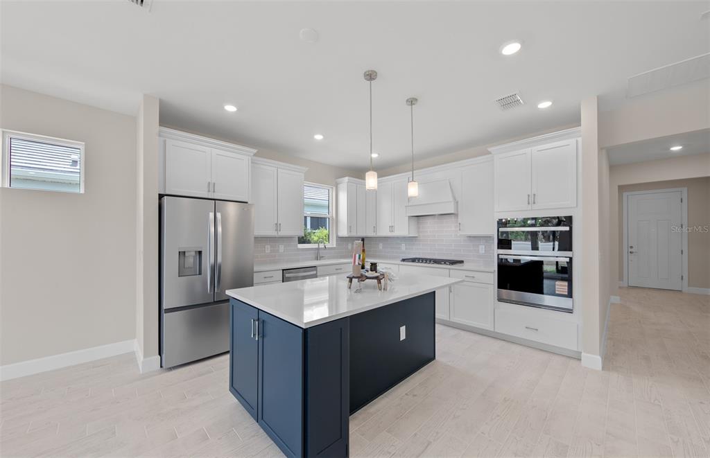A kitchen features white cabinetry, a dark blue island, stainless steel appliances, and light flooring — 1828 SILVER SHORES BOULEVARD, ENGLEWOOD, FL
