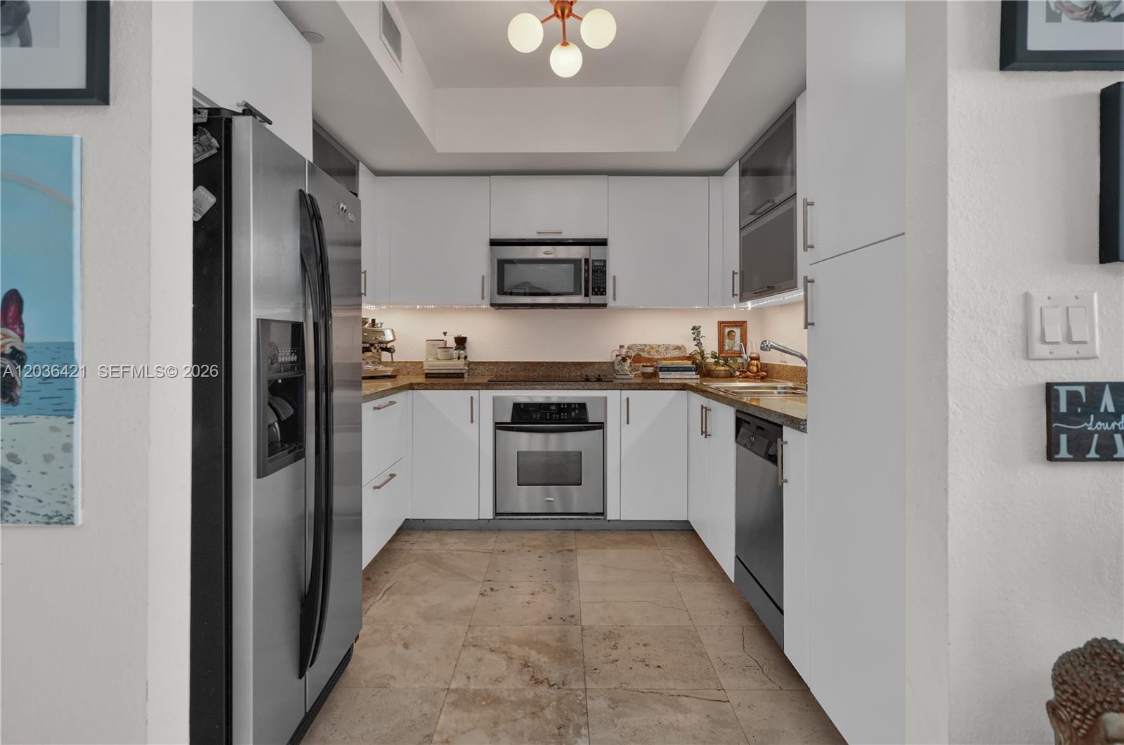 A modern kitchen features white cabinetry, stainless steel appliances, and tan stone floor tiles — 500 NE 29th St # 901, Miami FL 33137, MIAMI, FL