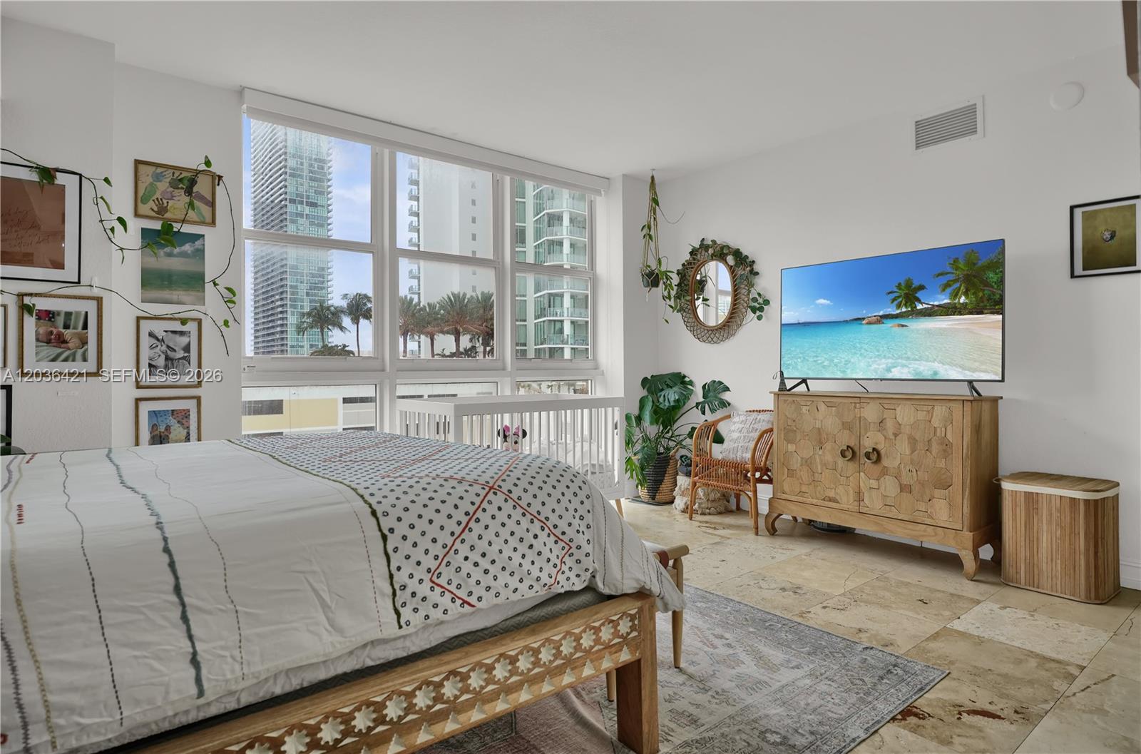 A bedroom features a bed, a crib, a television on a wooden cabinet, and floor-to-ceiling windows — 500 NE 29th St # 901, Miami FL 33137, MIAMI, FL