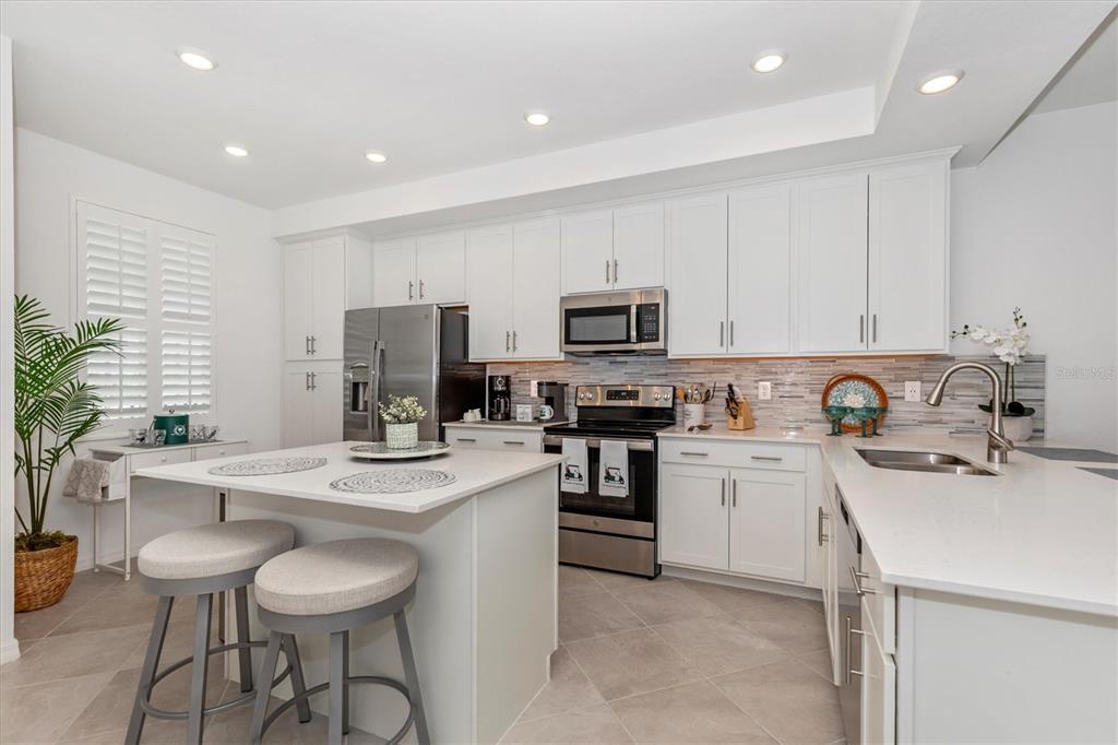 A modern kitchen features white cabinetry, stainless steel appliances, a center island, and tile flooring — 12280 WELLEN GOLF STREET UNIT 304, VENICE, FL
