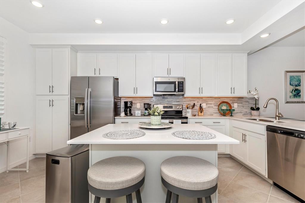 A modern kitchen features white cabinetry, stainless steel appliances, a central island, and tiled flooring — 12280 WELLEN GOLF STREET UNIT 304, VENICE, FL