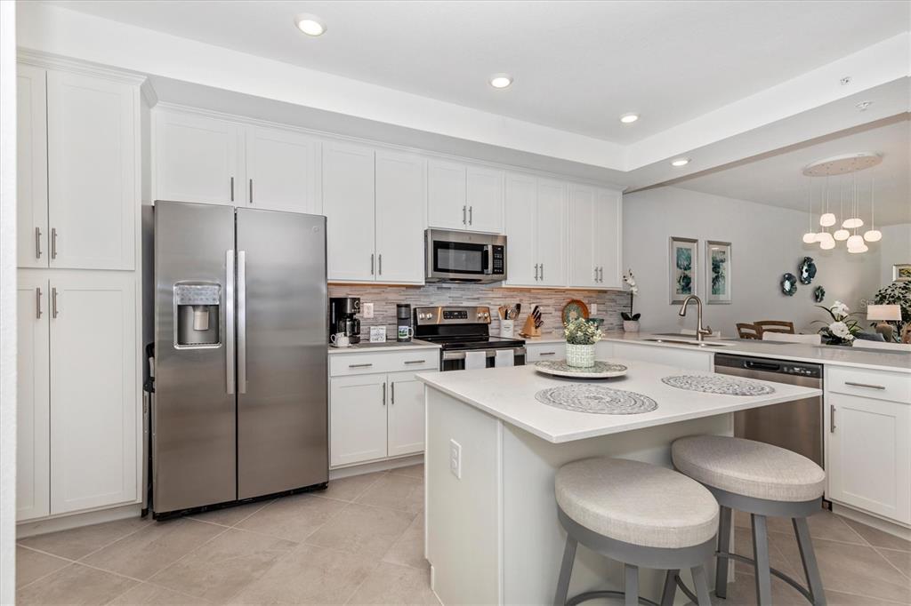 A modern kitchen features white cabinetry, stainless steel appliances, a center island, and tile flooring — 12280 WELLEN GOLF STREET UNIT 304, VENICE, FL