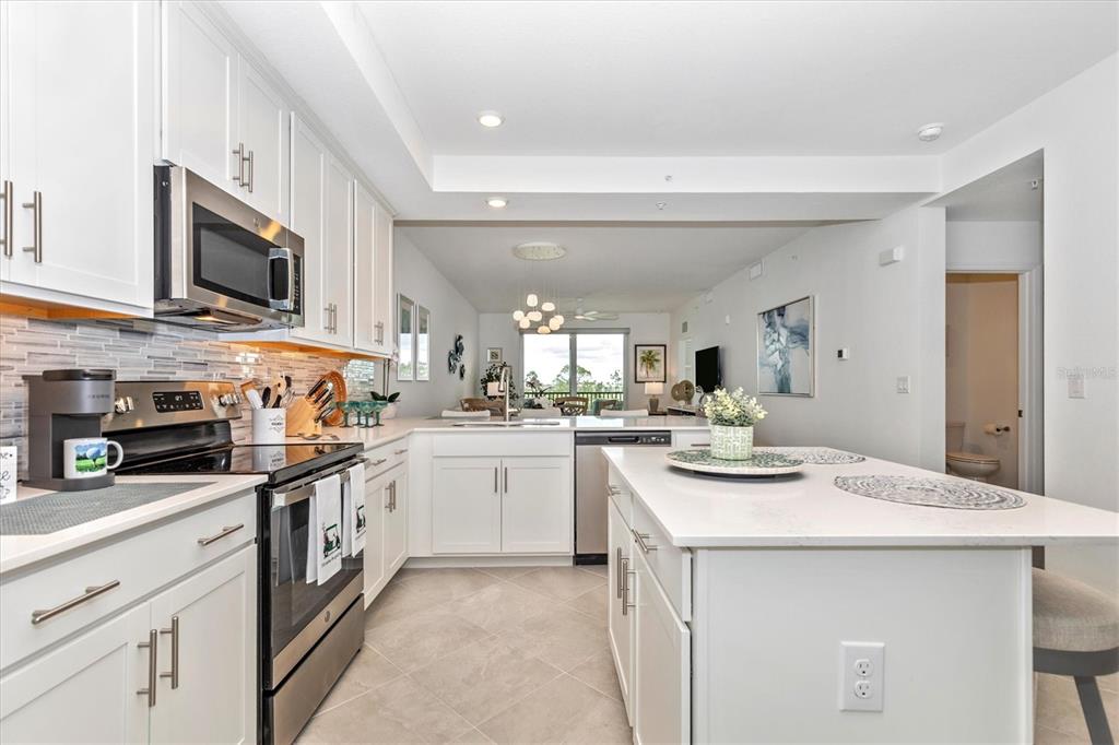 A modern white kitchen features stainless steel appliances, a center island, and an open layout — 12280 WELLEN GOLF STREET UNIT 304, VENICE, FL