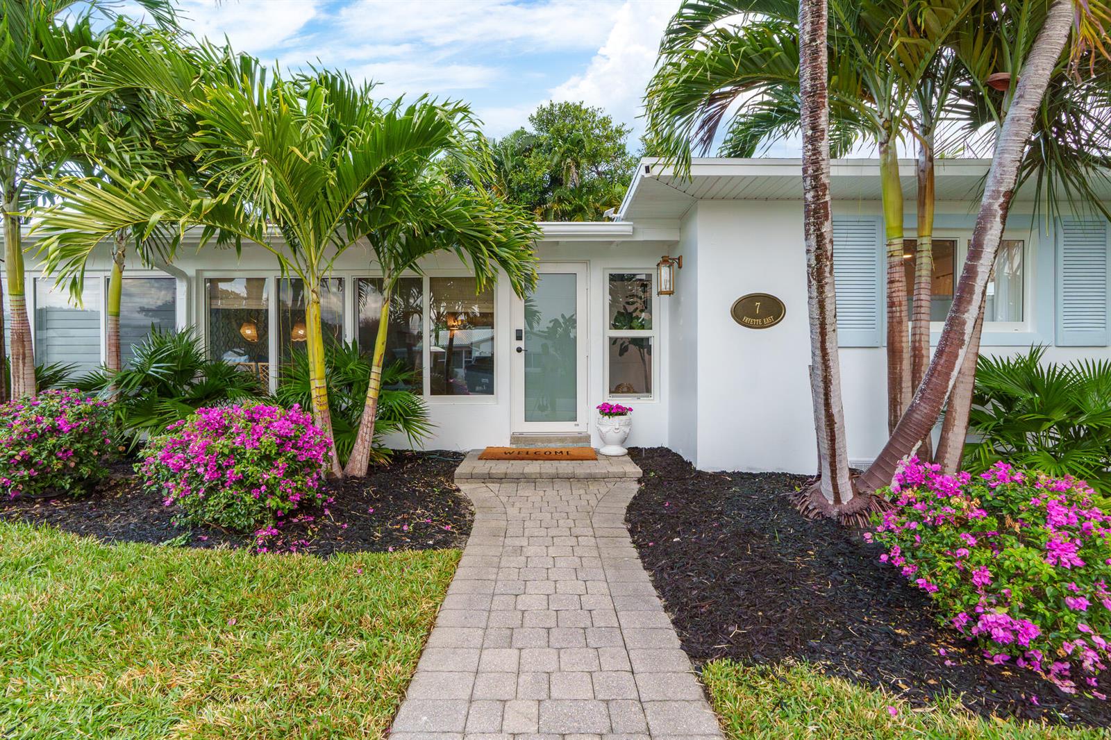 A paved walkway leads to the front entrance of a white house with palm trees — 7 Fayette Drive, Ocean Ridge FL 33435, OCEAN RIDGE, FL
