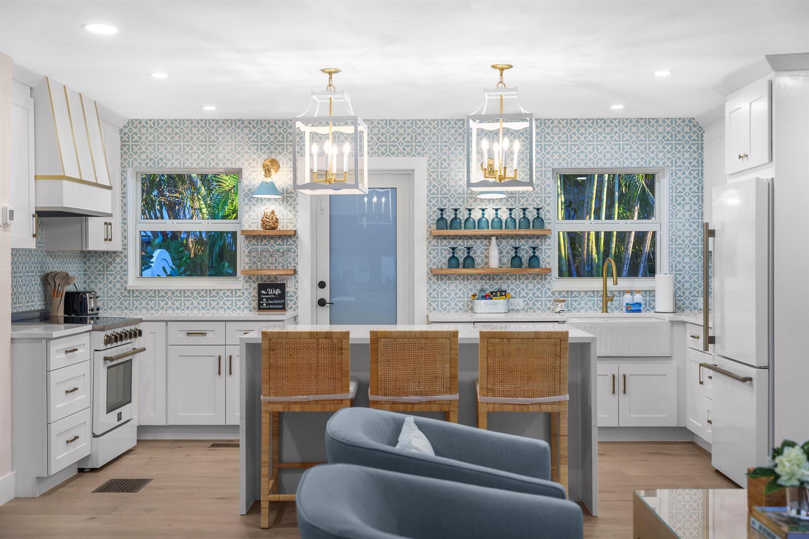 A bright kitchen features white cabinetry, a patterned blue backsplash, and a central island with stools — 7 Fayette Drive, Ocean Ridge FL 33435, OCEAN RIDGE, FL