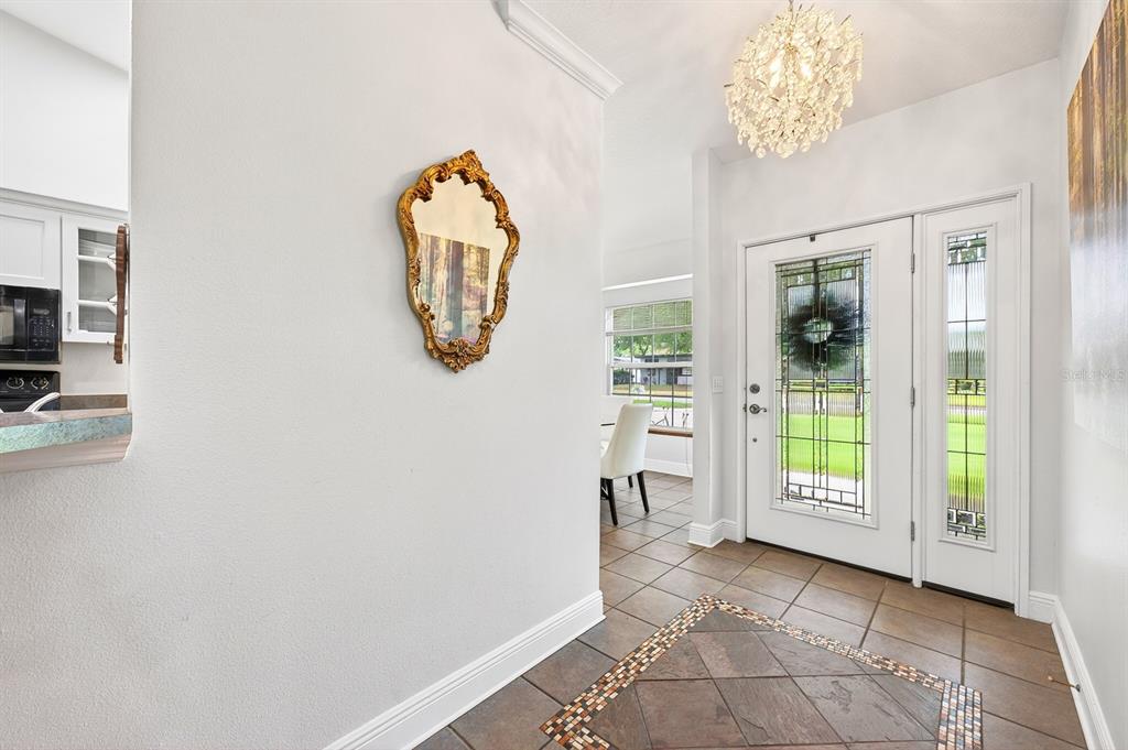 An entryway features a tiled floor, a gold-framed mirror, a chandelier, and a glass-paneled door — 2706 HARGILL DRIVE, ORLANDO, FL