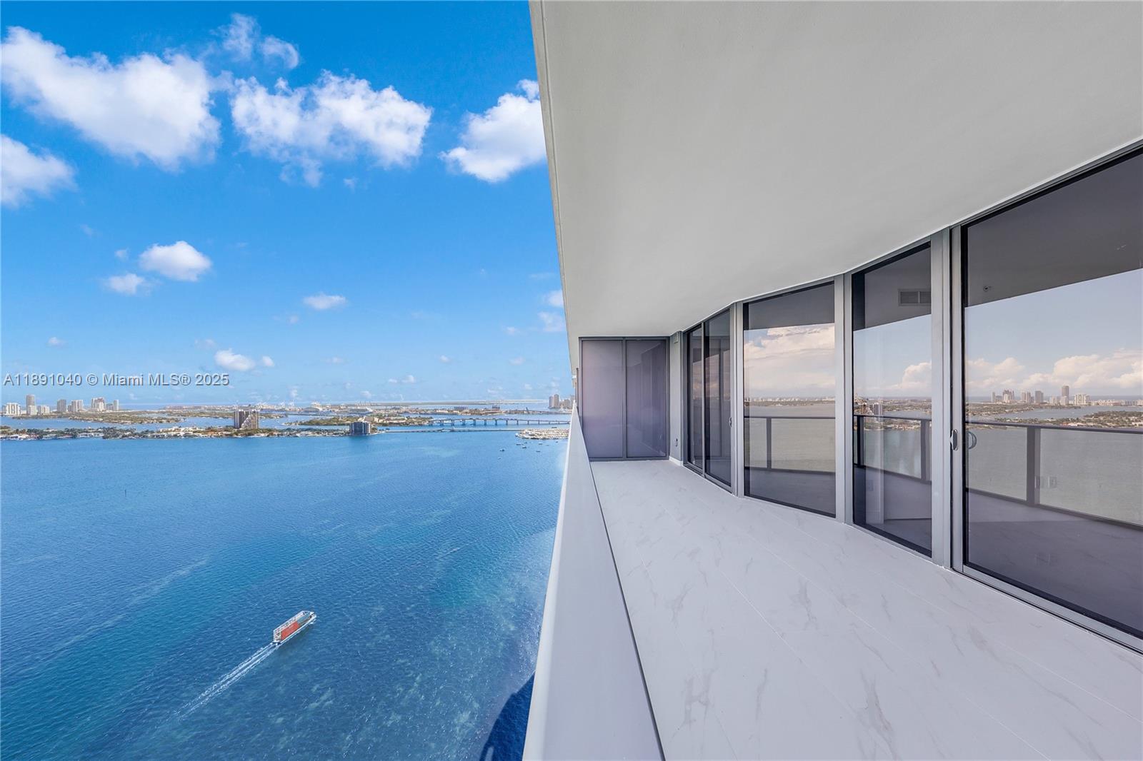 A high-rise balcony with white marble-look flooring overlooks a large bay and city skyline — 700 NE 24 St # 3402, Miami FL 33137, MIAMI, FL