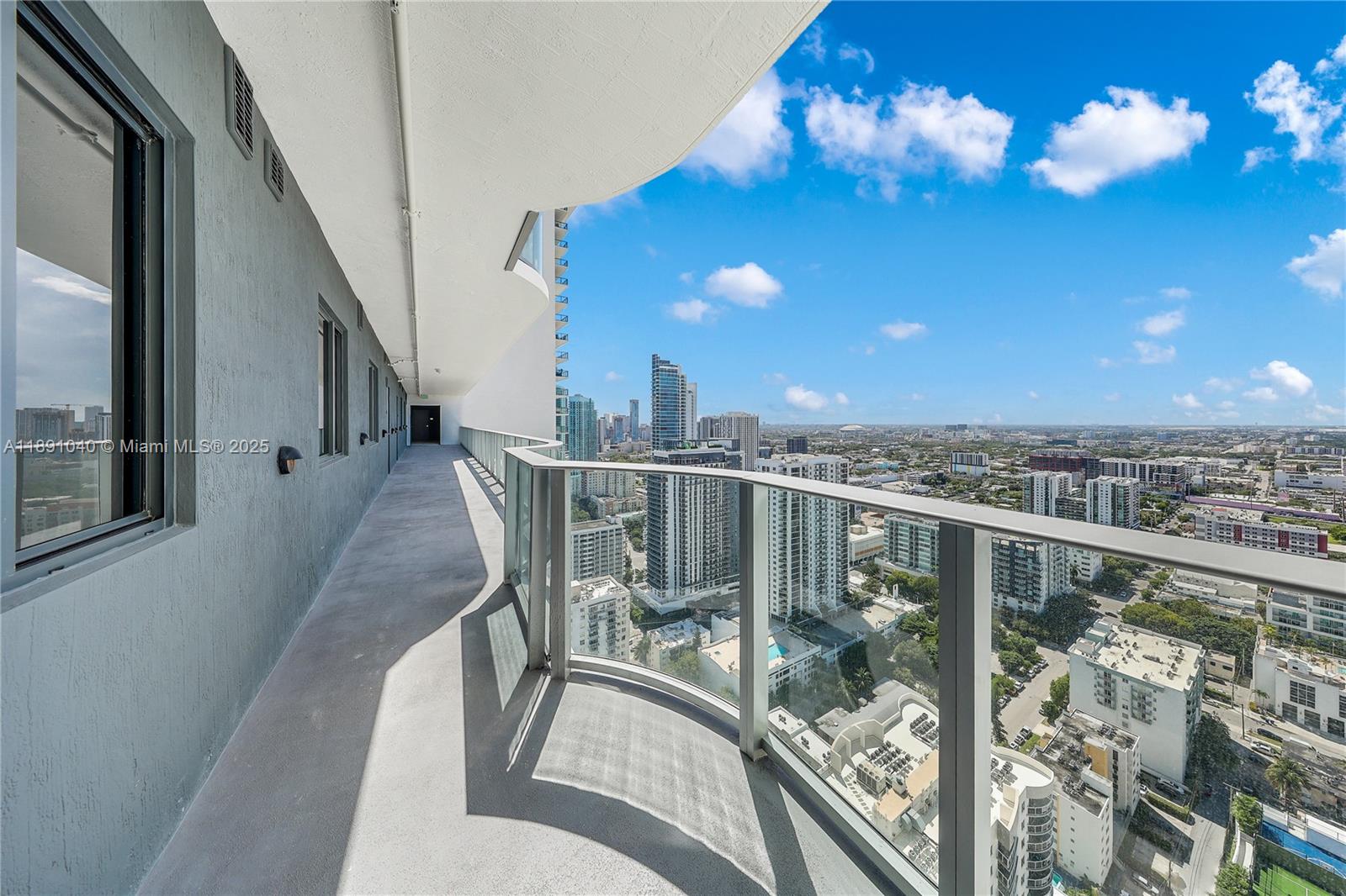 A high-rise balcony with a glass railing overlooks a dense urban cityscape under a blue sky — 700 NE 24 St # 3402, Miami FL 33137, MIAMI, FL