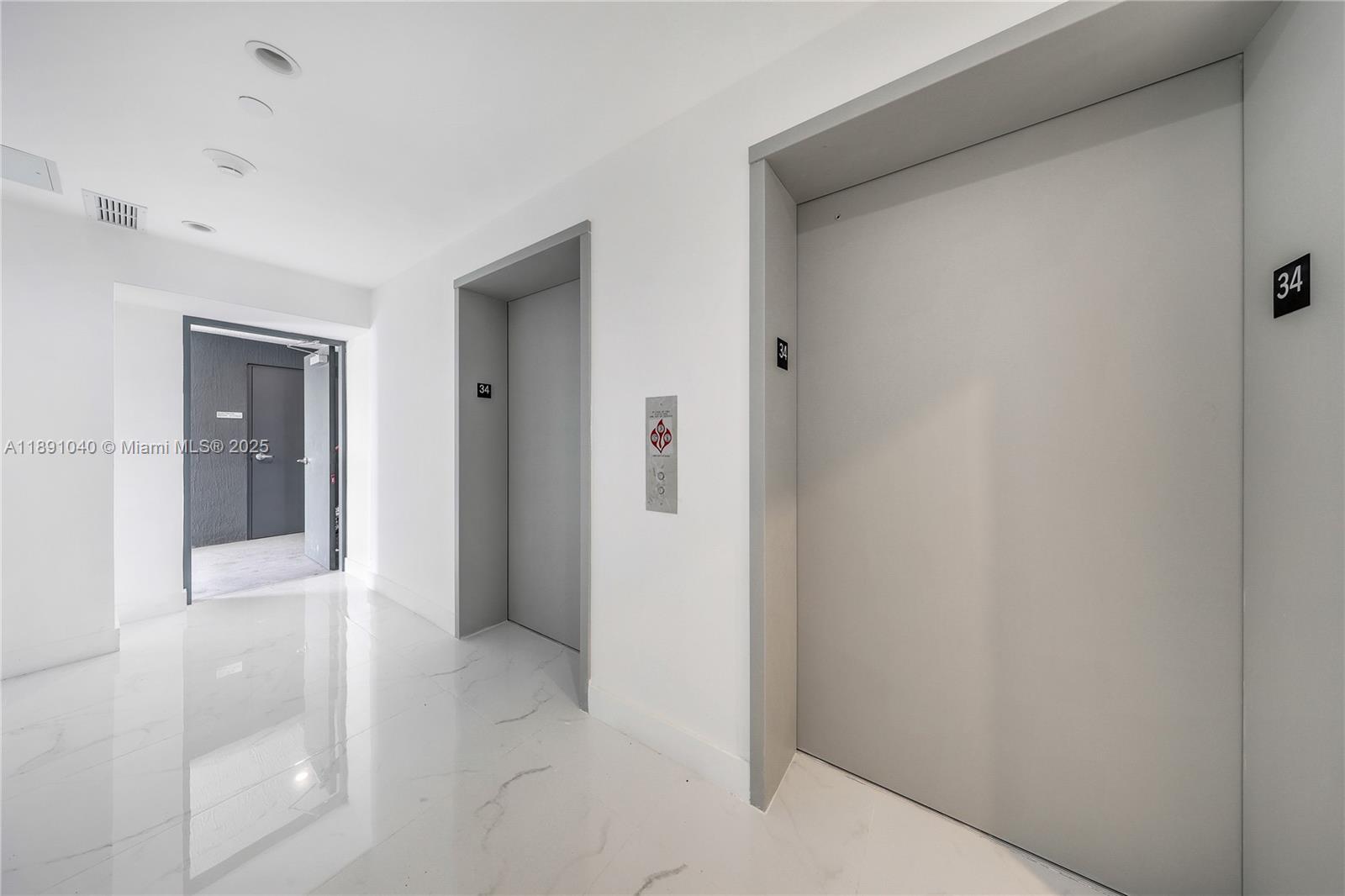A hallway features white marble floors, two gray elevator doors, and a dark doorway — 700 NE 24 St # 3402, Miami FL 33137, MIAMI, FL
