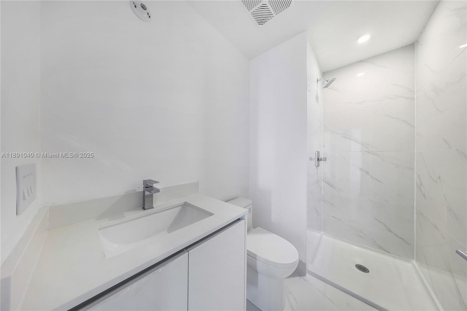 A modern bathroom features a white vanity, a toilet, and a glass-enclosed marble shower — 700 NE 24 St # 3402, Miami FL 33137, MIAMI, FL